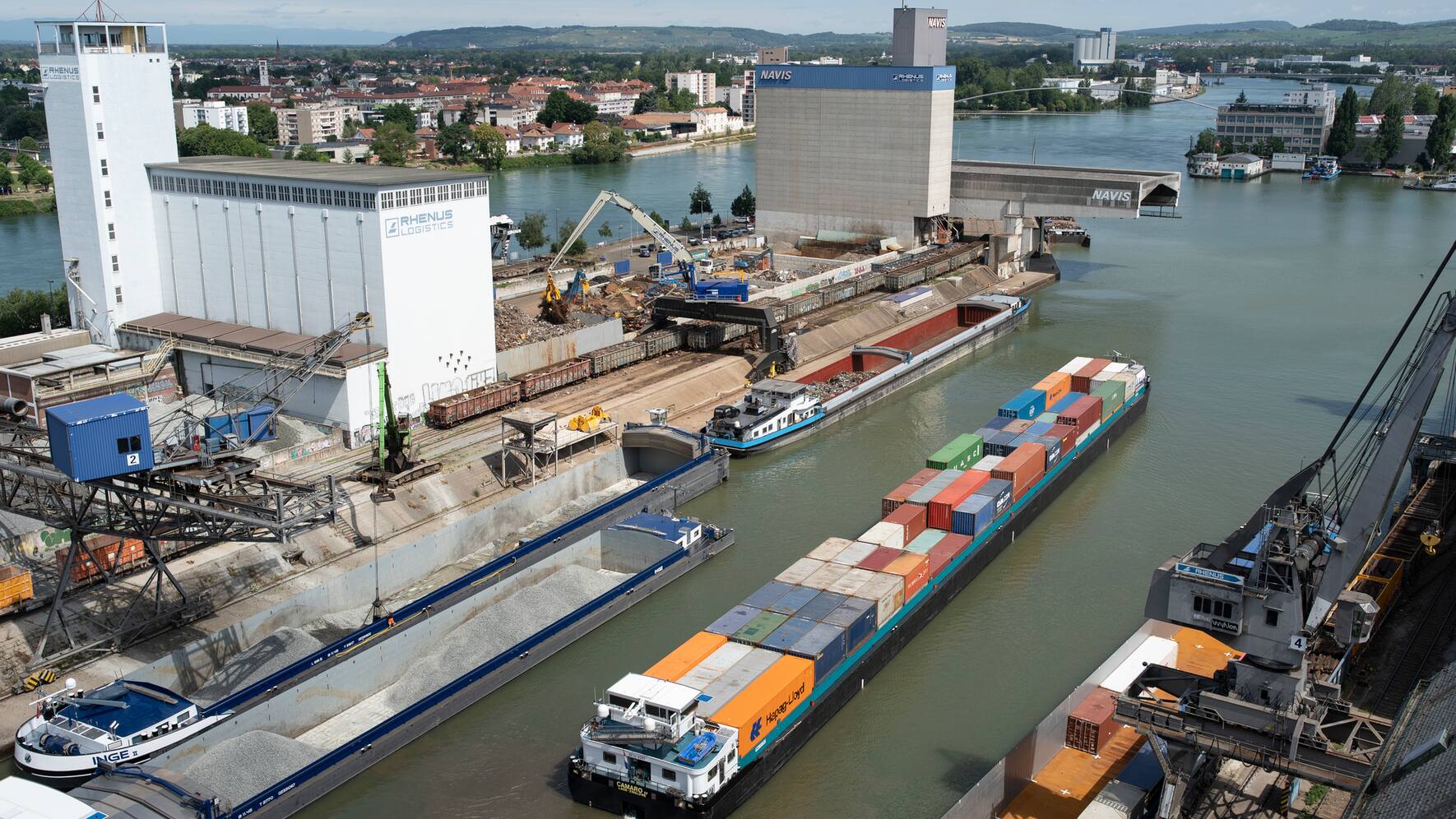 Ein Frachtschiff mit Schotter beladen faehrt in den Hafen ein, waehrend ein Containerschiff diesen in Richtung Norden verlaesst, fotografiert am 10. Juli 2020 am Port of Switzerland - Schweizerische Rheinhaefen in Basel-Kleinhueningen. (KEYSTONE/Gaetan Bally)