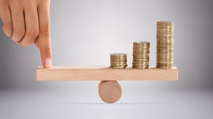 Close-up Of A Person's Finger Balancing Stacked Of Golden Coins On Wooden Seesaw Close-up Of A Person's Finger Balancing Stacked Of Golden Coins On Wooden Seesaw