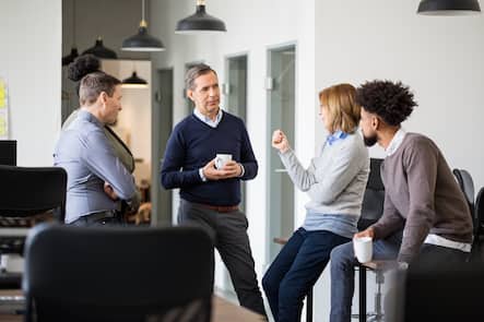 Fünf Personen unterschiedlichen Alters diskutieren miteinander im Büro.