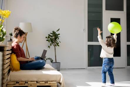 Mother sitting on couch working with laptop while daughter is playing with balloon model released, Symbolfoto property released, JOSEF09422