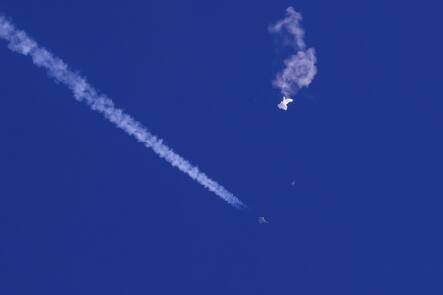 In this photo provided by Chad Fish, the remnants of a large balloon drift above the Atlantic Ocean, just off the coast of South Carolina, with a fighter jet and its contrail seen below it, Saturday, Feb. 4, 2023.