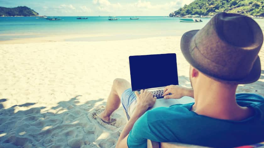 Attractive young man with laptop working on the beach. Freedom, remote work, freelancer, technology, internet, travel and vacation concepts