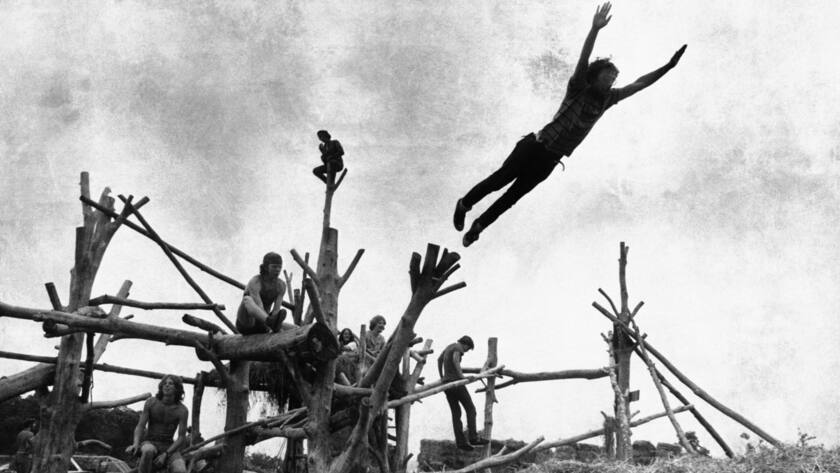 Rock music fans sit on a tree sculpture as one leaps mid-air onto a pile of hay during the Woodstock Music and Art Festival held on a cow pasture at White Lake in Bethel, New York on Aug. 15, 1969. (AP Photo)