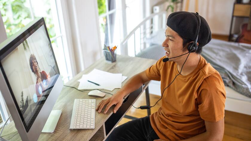 Ein junger Mann sitzt vor dem PC und chattet per Video mit einer Frau.