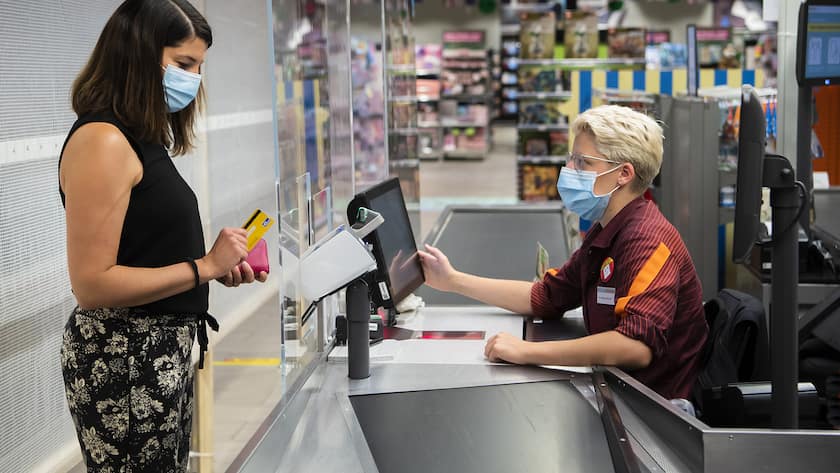 Kundin mit Schutzmase bezahlt an der Migros-Kasse