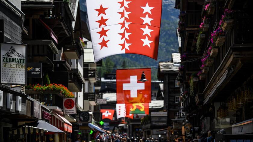 Des touristes visitent la rue centrale du village de montagne sous le drapeau du canton du Valais et sous le drapeau Suisse le vendredi 17 juin 2022 a Zermatt. (KEYSTONE/Jean-Christophe Bott)
