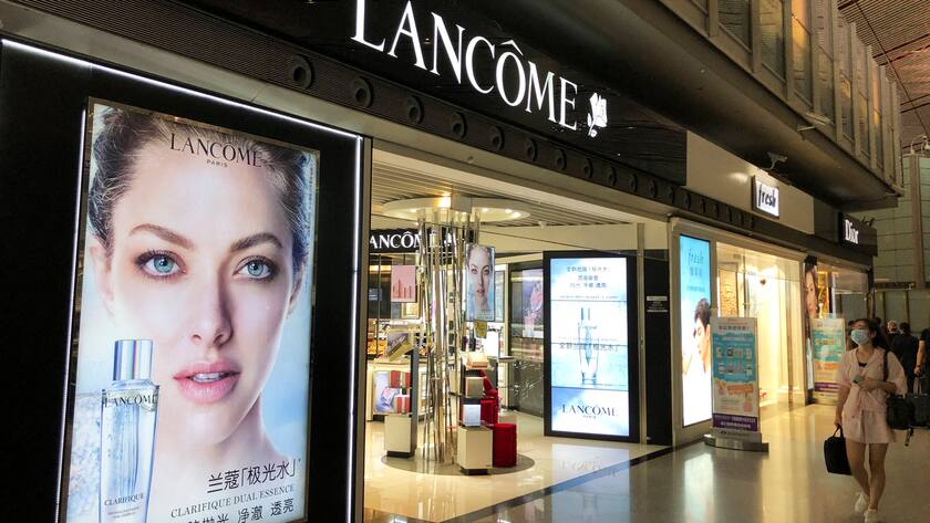 Ein Laden der Kosmetikmarke Lancome in einem Flughafen. Eine Frau läuft daran vorbei und schaut sich die Werbung an.