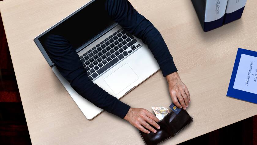 Arme, die aus einem Laptop kommen und Geld stehlen, das auf Bürotisch liegt