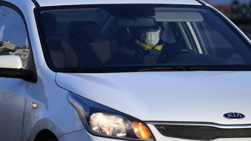Person mit Maske am Steuer eines Kia-Autos.
