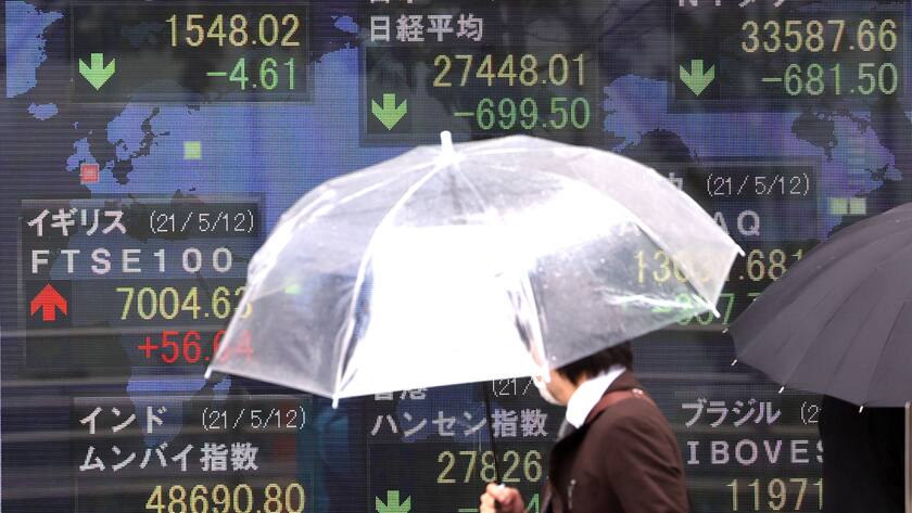 Ein Mann mit Regenschirm steht vor Bildschirmen in Tokyo, die Kursverläufe anzeigen.