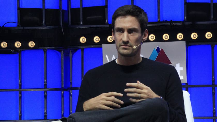 Guillaume Pousaz sitzt in einem Stuhl und hat die Beine überschlagen. Er trägt ein Mikrophon und spricht.