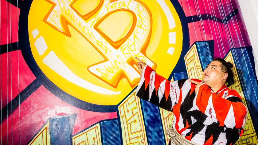 Der japanische Sumo-Ringer Sumo Yama posiert vor einem Bitcoin-Wandbild.