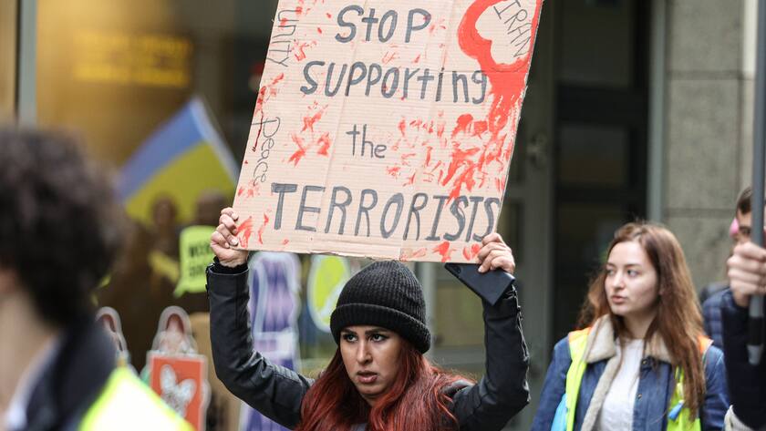 Tausende bei Ukraine- und Iran-Demo in Köln. Eine schwarz gekleidete Frau hält ein Schild in die Höhe, darauf steht: Stoppt die Unterstützung von Terroristen.