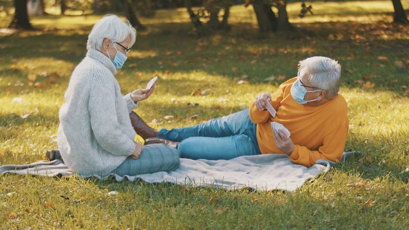 Anniversary celebration in the park during covid-19. Elderly couple with face mask having funny picnik in autumn. High quality photo