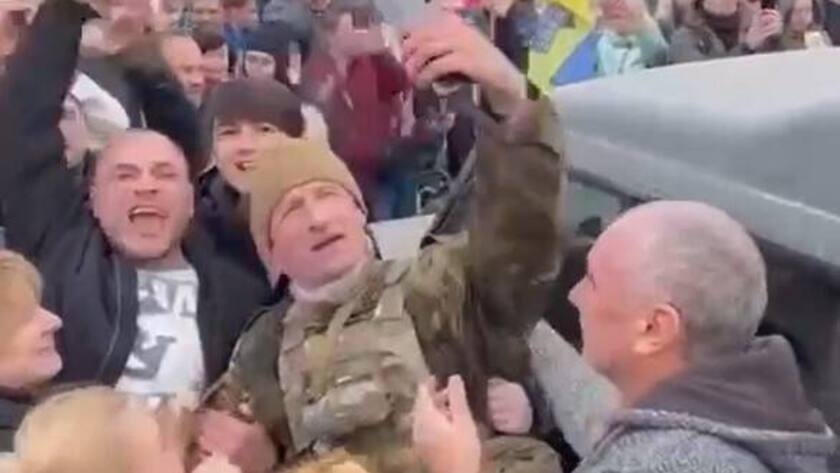 Soldat in der Mitte einer Menschenmenge macht ein Foto, einige Leute applaudieren.