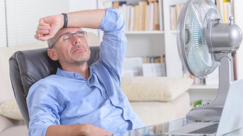 Man suffers from heat while working in the office and tries to cool off by the fan