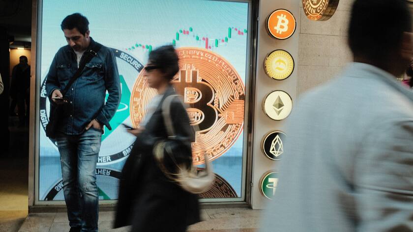 Personen gehen an grosser Bitcoin Werbung vorbei.