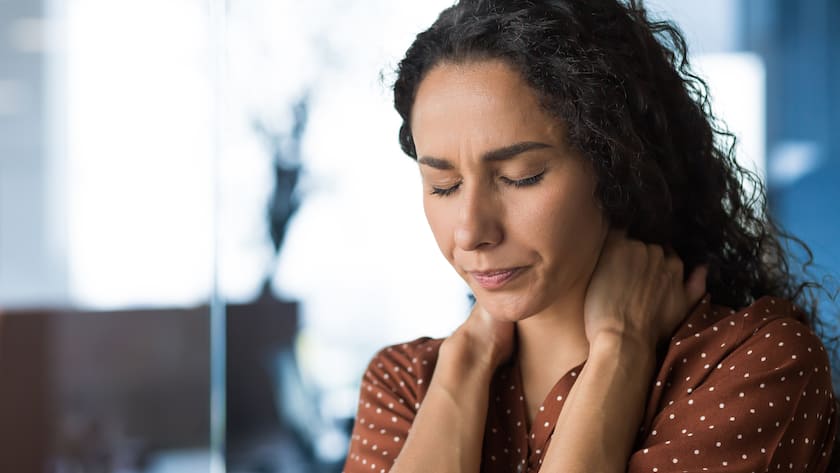 Psychische Erschöpfung - übermüdete Frau am Arbeitsplatz - Krankheitng in modern office businesswoman has severe neck pain, massages neck muscles, business woman in casual clothes and curly hair.