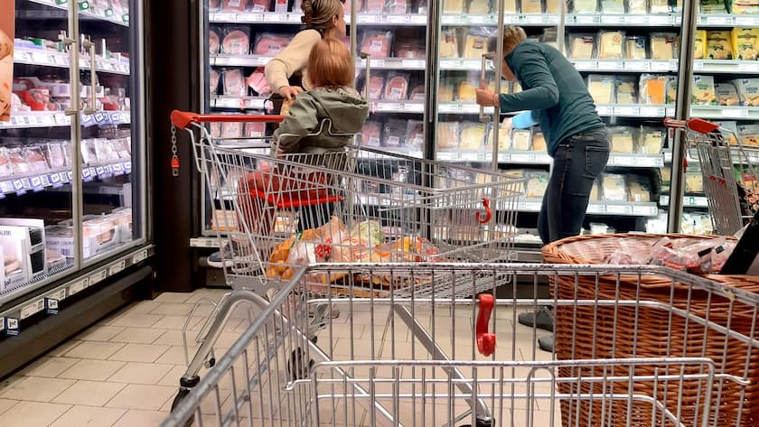 Einkauf in einem Supermarkt oder Discounter in Deutschland. Im Vordergrund ist ein Einkaufswagen dahinter zwei Personen am Kühlregal.