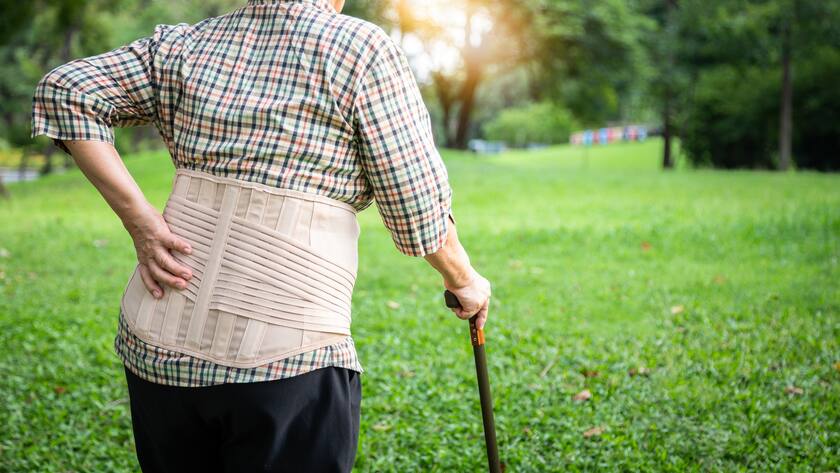 Asian senior woman wearing back support belt for protect her back pain,muscle injury,elderly people hand touching on the hip having lumbago pain,backache,suffering from waist pain in outdoor nature at park