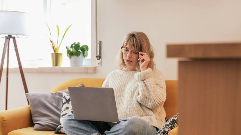 Woman in glasses sitting on a couch and using a laptop