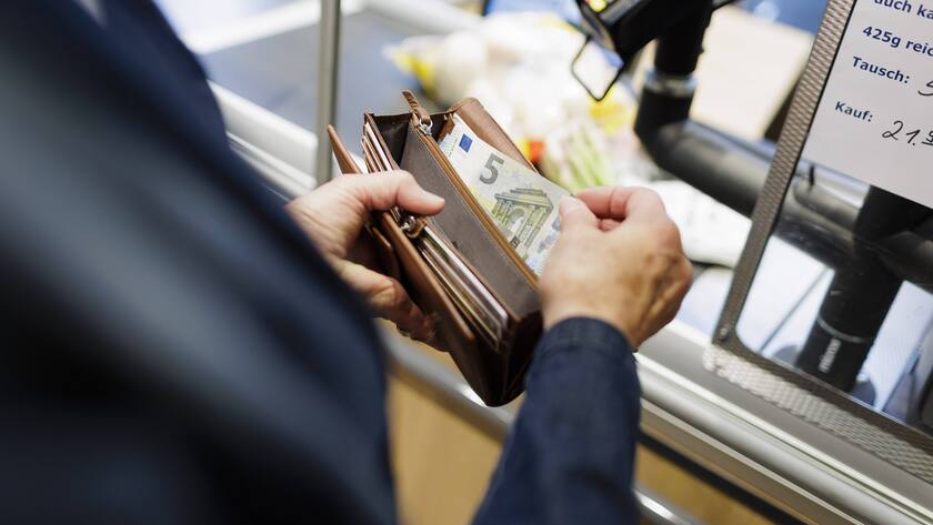 Eine Person zieht fünf Euro Schein aus dem Portemonnaie.