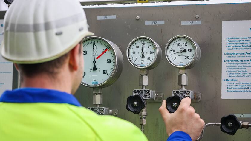 Bauarbeiter von hinten mit weissem Helm und gelber Leuchtweste an einem Erdgasregler in Deutschland.
