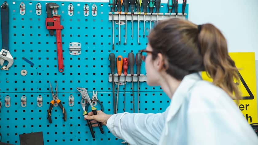 Frau greift nach Werkzeug in einer Werkstatt.
