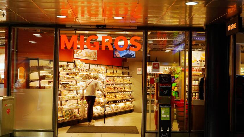 Ein Migros Eingang mit einer alten Dame die hineinspaziert.