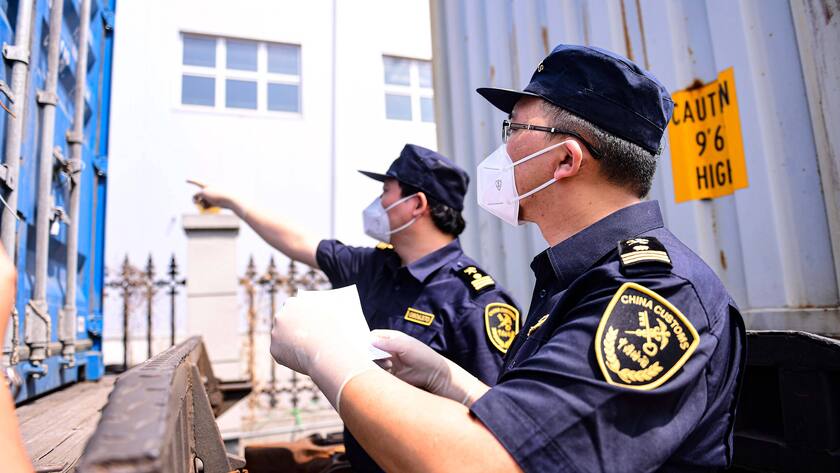 Zwei chinesische Zollbeamte mit Maske untersuchen einen Container.