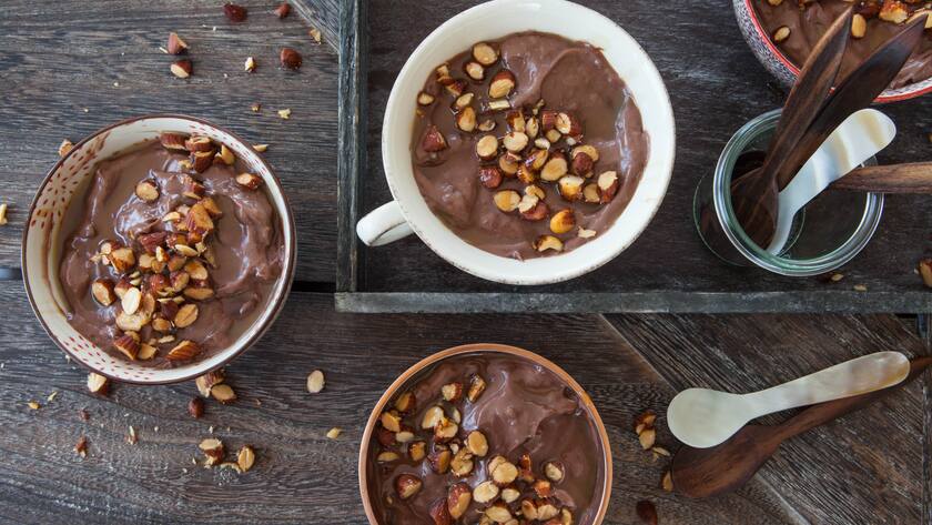 Drei Schalen Kakao-Pudding, garniert mit Nüssen, auf einem Holztisch.