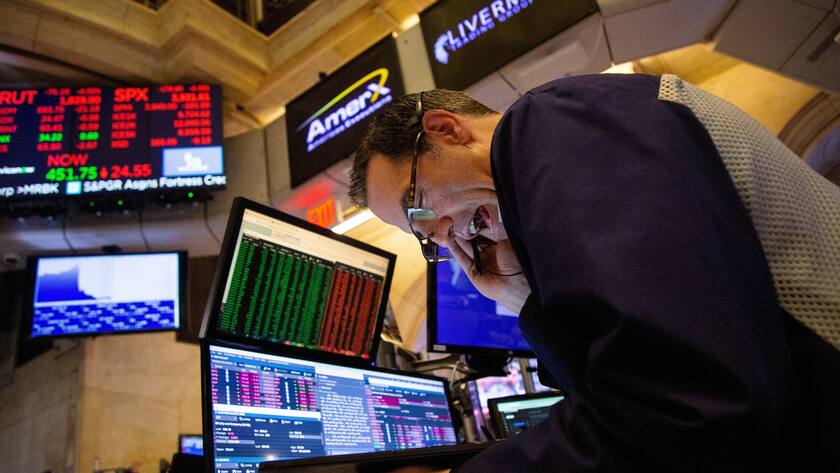 Ein Mann an der US-Börse am Telefon vor mehreren Bildschirmen mit Aktienkursen drauf.