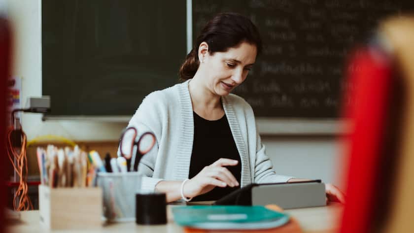 Lehrerin sitzt am Pult und korrigiert Arbeiten.
