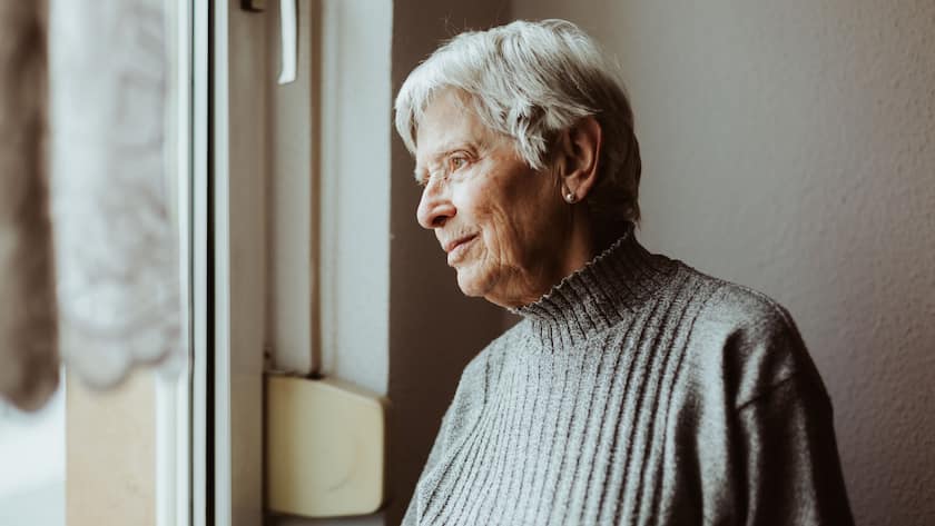 Eine Seniorin schaut nachdenklich aus dem Fenster.