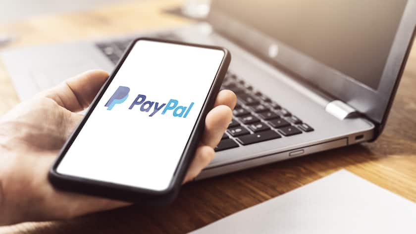 Paypal Online Zahlungsservice und Banking Unternehmen auf einem Smartphone Display, das in der Hand vor einem Notebook auf einem Tisch gehalten wird Paypal Online Payment (KEYSTONE/CHROMORANGE/Michael Bihlmayer)