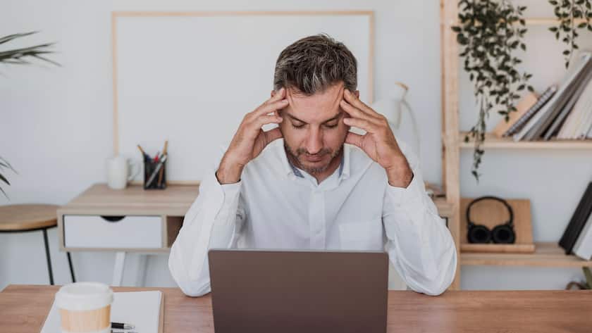 Gestresster Mann vor einem Bildschirm mit den Händen an den Schläfen zum Massieren