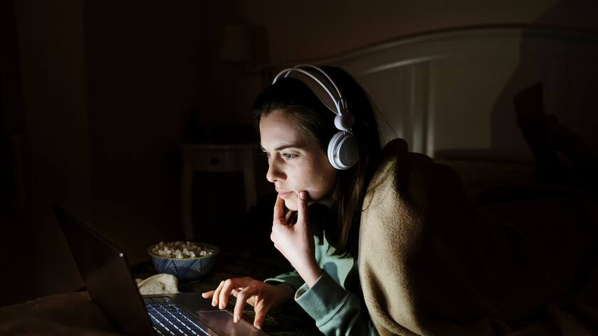Young woman wearing headphones watching movie on laptop while resting on bed at home model released Symbolfoto property released AFVF08208