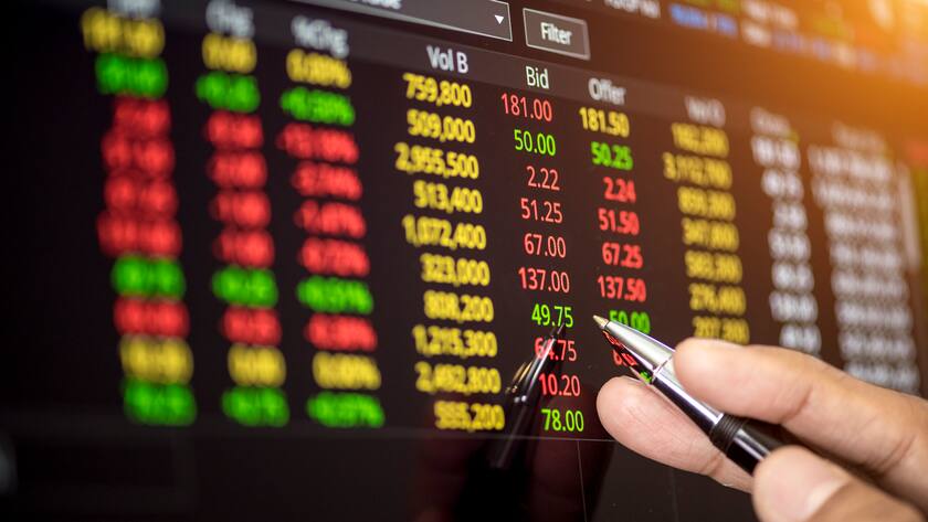 Hand holding pen pointing to stock market graph on screen