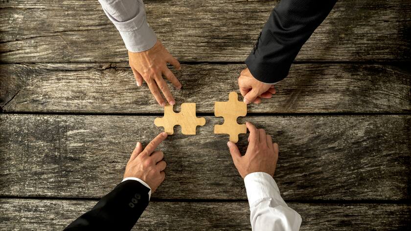 Four successful business men joining two puzzle pieces each being held by two partners, rustic wooden background. Conceptual of merger or creative cooperation of two business companies.