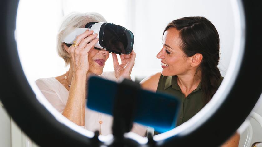 Smiling woman looking at grandmother wearing virtual reality simulator while vlogging at home model released Symbolfoto property released OIPF00950