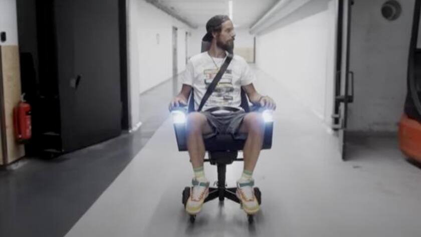 Junger Mann im Bürostuhl von VW mit Sicherheitsgurte und Licht fährt durch eine Tiefgarage.