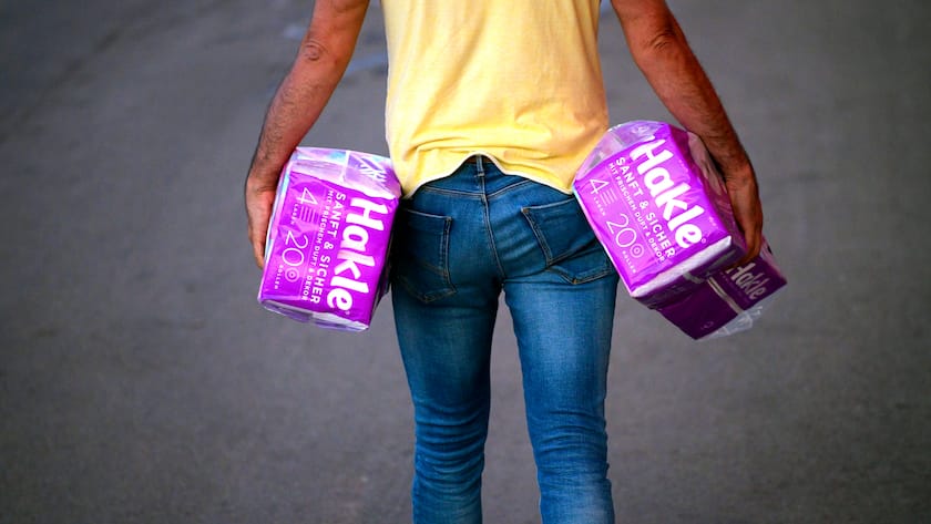 Mann läuft mit zwei Packungen Klopapier von Hakle.