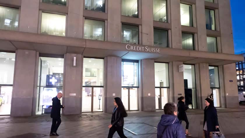 Credit Suisse Gebäude in Genf beim Eindunkeln, davor gehen Personen hin und her.