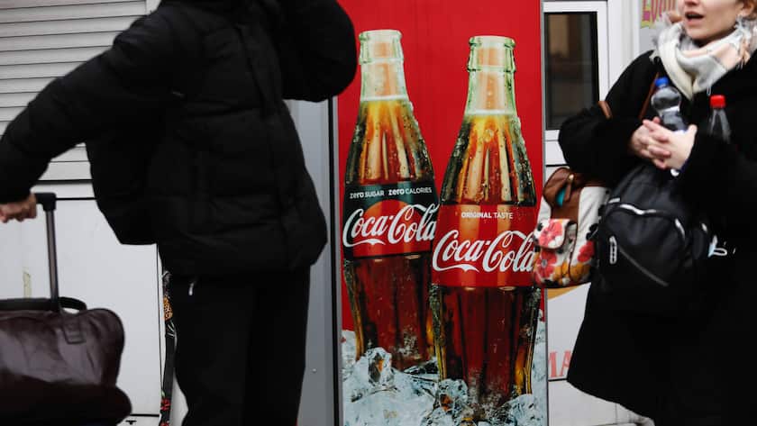 Coca Cola Logo auf Getränkeautomat mit zwei Reisenden im Vordergrund