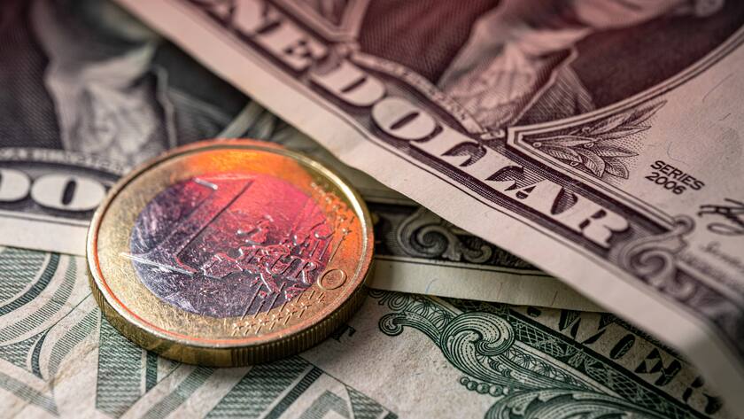 Eine Euromünze liegt auf ein-Dollar-Noten.