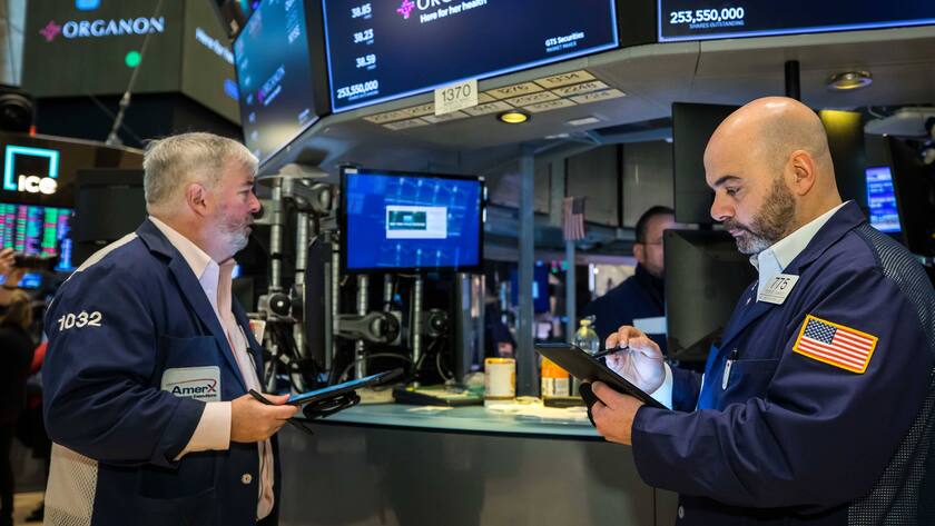 Zwei Männer in New York Börse mit Tablets in der Hand vor Bildschirmen mit Aktiendaten.