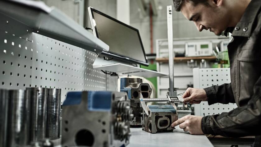 Worker in metalworking factory measuring cylinder head with caliper