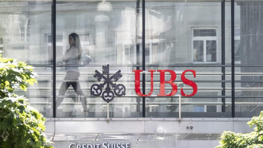 Ein Frau laeuft zwischen den beiden Logos der Banken UBS und Credit Suisse, aufgenommen am Montag, 12. Juni 2023 in Zuerich. Heute verkuendete die nunmehr einzige Schweizer Grossbank in einem offenen Brief: Die Uebernahme der Credit Suisse durch die UBS ist vollzogen. (KEYSTONE/Ennio Leanza)
