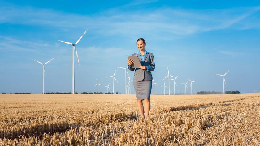 Women putting money into an ethical Investment of wind turbines, standing with her computer on a field