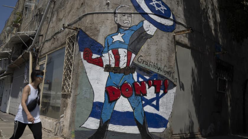 A woman walks past a mural depicting U.S. President Joe Biden as a superhero defending Israel on a street in Tel Aviv, Israel, Sunday, April 14, 2024.
